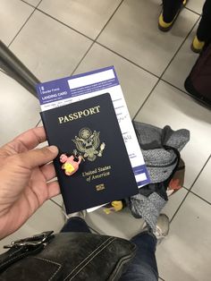 a person holding a passport in their left hand and luggage on the ground behind them