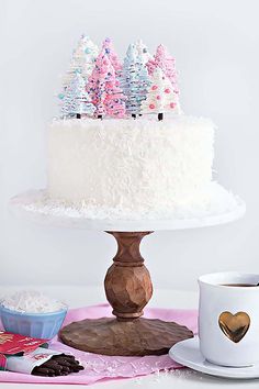 a white cake with pink and blue frosting trees on top next to a cup of coffee