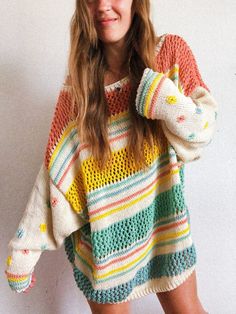 a woman wearing a multicolored sweater poses in front of a white wall with her hands on her head