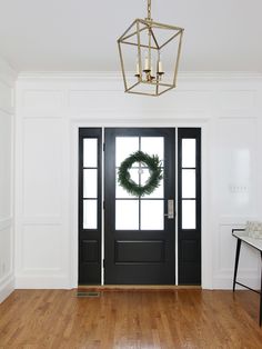 a black front door with a wreath hanging on it's side and an entry way