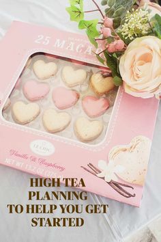 a pink box filled with heart shaped cookies on top of a white table next to flowers