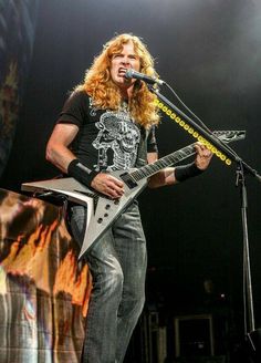 a man with long hair playing an electric guitar on stage at a music festival or concert