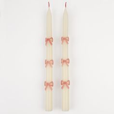 two candles with bows on them sitting side by side against a white background, one is lit and the other has pink ribbon