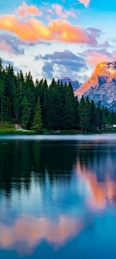 the mountains are reflected in the still water of this lake at sunset, with pine trees on both sides