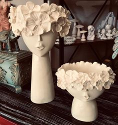 two white vases with flowers in them sitting on a table next to other figurines