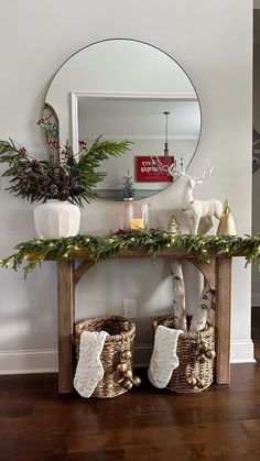 a wooden table topped with baskets filled with christmas decorations next to a mirror and potted plants