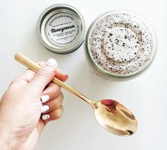 a hand holding a spoon next to a jar of whipped cream on a white surface