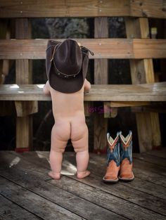 a small baby standing next to a pair of cowboy boots on top of a wooden bench