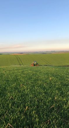 a tractor is driving through the middle of a large field with green grass in front of it