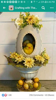 an easter decoration with yellow flowers and eggs in a white egg shaped vase on top of a pedestal