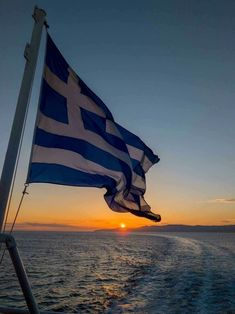 the sun is setting over the water as seen from a boat in the ocean with a greek flag