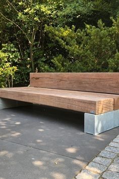 a wooden bench sitting on top of a stone walkway next to trees and bushes in the background