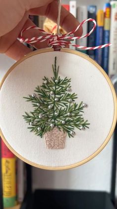 a hand embroidered christmas tree ornament hanging from a string in front of a bookshelf