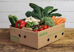 a cardboard box filled with fresh vegetables on top of a wooden table