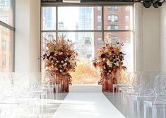 Modern City Wedding with Tall Autumn Florals and Clear Acrylic Chairs – Elegant skyscraper rooftop wedding ceremony featuring bold orange, yellow, and burgundy floral arrangements with sleek acrylic seating. Perfect for an urban fall wedding!