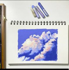 three markers are sitting on top of a drawing book next to some pens and watercolors