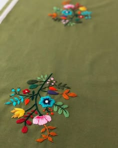 an embroidered tablecloth with flowers and leaves on green fabric, close up view from the top