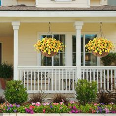 two hanging baskets filled with yellow flowers on the front porch of a white house,