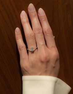 a woman's hand with a diamond ring on her left hand, against a wood background