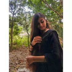 a woman with long hair standing in the woods wearing a black dress and bracelets