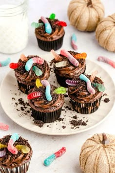 chocolate cupcakes decorated with candy and candies on a plate next to pumpkins