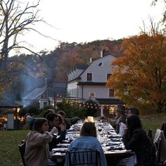 a group of people sitting around a long table with food on it in front of a house