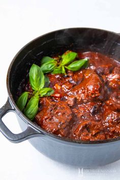 meatballs with tomato sauce and basil in a black skillet on a white surface