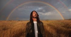 a man standing in the middle of a field with a double rainbow behind his head