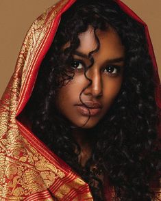 a woman with long curly hair wearing a red and gold shawl over her head