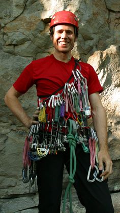 a man standing in front of a rock wall wearing a helmet and harness with lots of tools attached to it