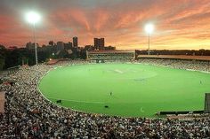 a baseball stadium filled with lots of people watching the sun go down in the distance