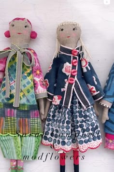 three cloth dolls are lined up against a white wall