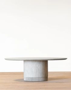 a white table with a round base on a wooden floor in front of a white wall