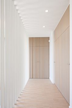 an empty hallway with white walls and wooden flooring is seen in this image from the side