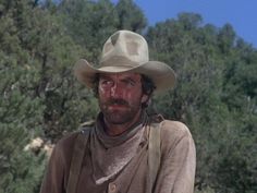 a man in a cowboy hat standing next to some trees