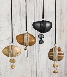 three different colored rocks hanging from strings on a white wooden wall with black cord and glass bead necklaces