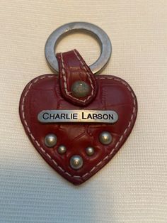 a red leather heart shaped keychain with a name tag attached to the front