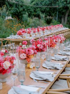 a long table is set with pink and white flowers in vases, plates and napkins