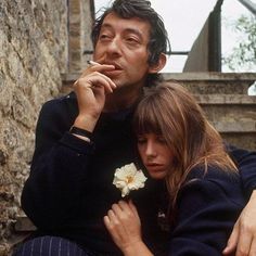 a man and woman sitting next to each other in front of a stone wall with stairs