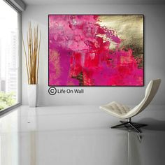 an abstract painting in pink and gold on a white wall next to a modern chair