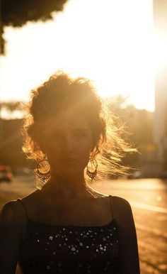 a woman standing on the street with her hair blowing in the wind and sun shining behind her