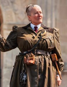 an older man in a trench coat and tie holding his hand out to the side