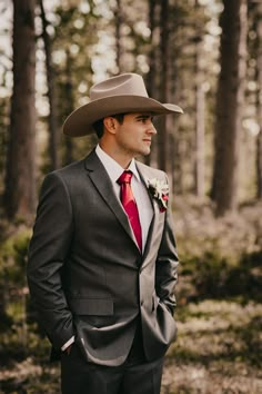 a man in a suit and red tie wearing a cowboy hat standing in the woods