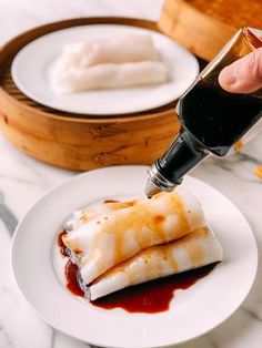 someone is dipping sauce onto some food on a plate with another dish in the background