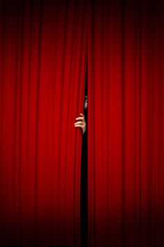 a hand peeking out from behind a red curtain