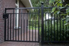 an iron gate is shown in front of a brick house with trees and bushes behind it