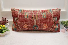 a red pillow sitting on top of a white floor next to a potted plant