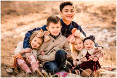 a man sitting on the ground with three children in front of him and smiling at the camera