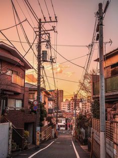 an empty street with power lines above it and buildings in the background at sunset or dawn