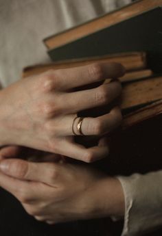 a woman holding a book with her hands on top of it and wearing a wedding ring